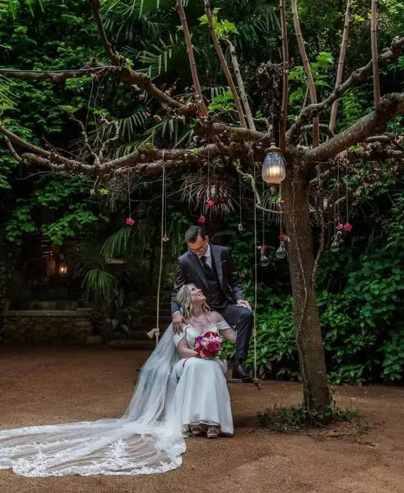 Pareja de novios en un columpio bajo un árbol decorado en el jardín de la finca La Vinyassa.