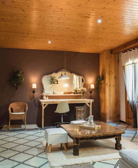Interior de una habitación amplia con techo de madera, tocador clásico con espejo, mesa de centro rústica y alfombra geométrica.
