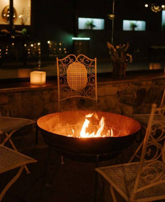 Brasero de metal encendido con fuego rodeado de sillas de hierro forjado en una terraza de piedra por la noche.