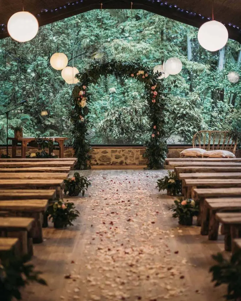 Espacio cubierto para ceremonias y bodas en la naturaleza, protegido de la lluvia con arco de flores, bancos de madera y vistas al bosque